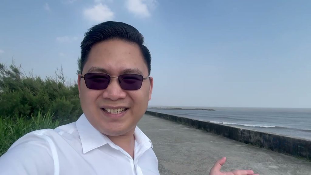 Nguyễn Ngọc trên đê biển Giao Ninh, con đê bê tông uốn cong dọc bờ biển, bên phải là biển, bên trái là hàng cây xanh