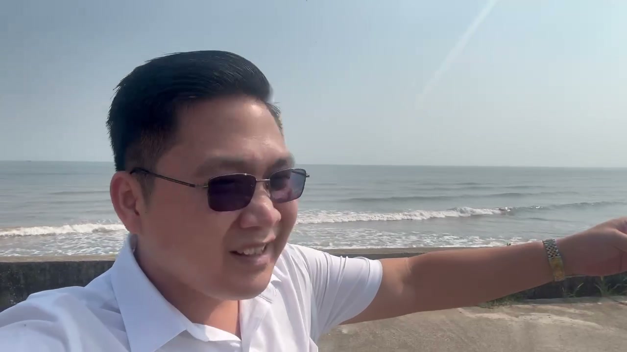 Nguyễn Ngọc đứng trên đê biển Giao Ninh, phía sau là sóng biển và bờ kè bê tông kéo dài